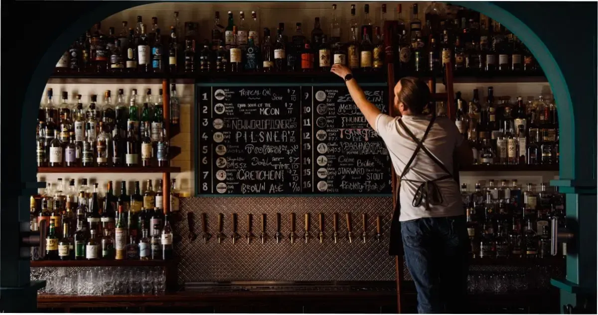 A bartender on a ladder, reaching for a bottle at an Adelaide Whisky Bar