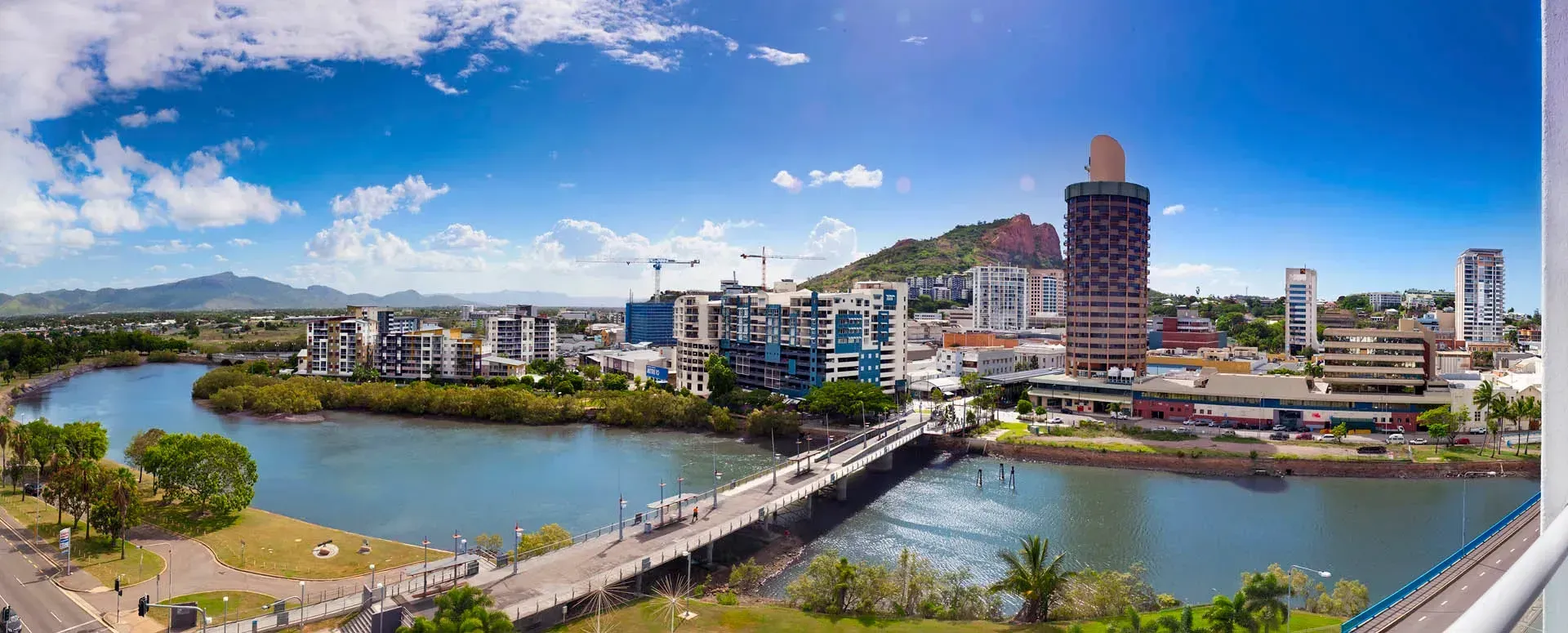 Aerial view of a city with a river, bridge, and skyline on a sunny day.