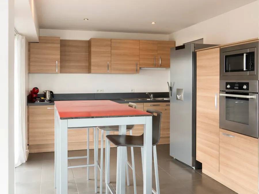Modern kitchen with dining table and appliances in two-bedroom apartment at Appart’Hôtel Hévéa, Valence.