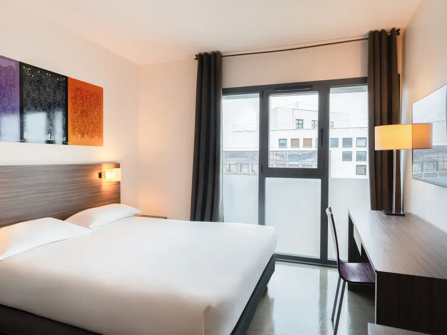 Superior Studio room with a large bed, desk, and large window at Appart’Hôtel Hévéa in Valence.