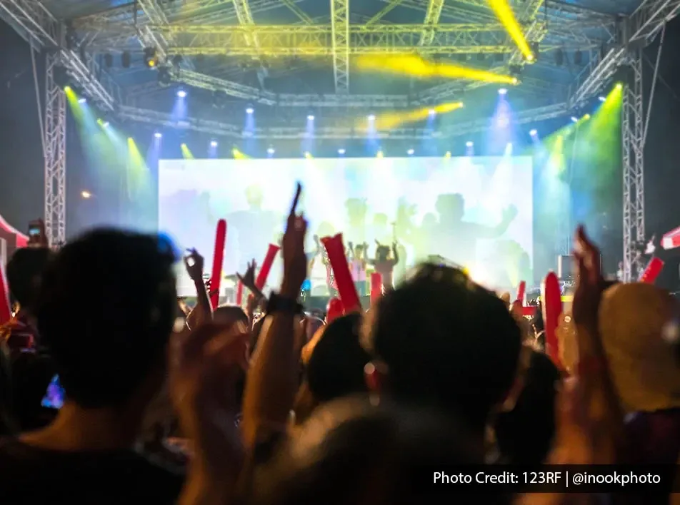 Crowd cheering at a live concert with colourful stage lights