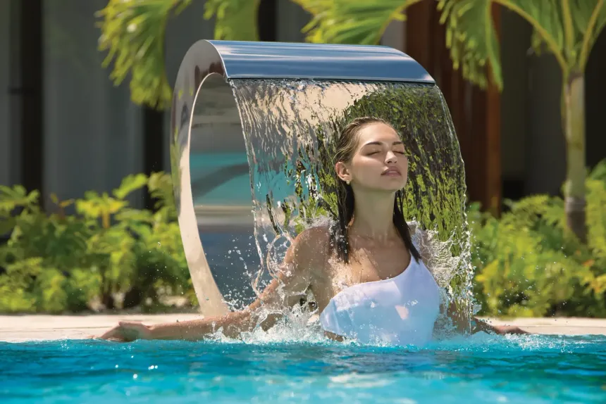 Woman relaxing under a beautiful water feature in the outdoor pool at Saint Martin Beach Hotel
