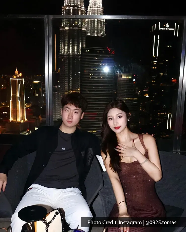 A couple seated at a restaurant, posing for a photo with KLCC skyline during night time.