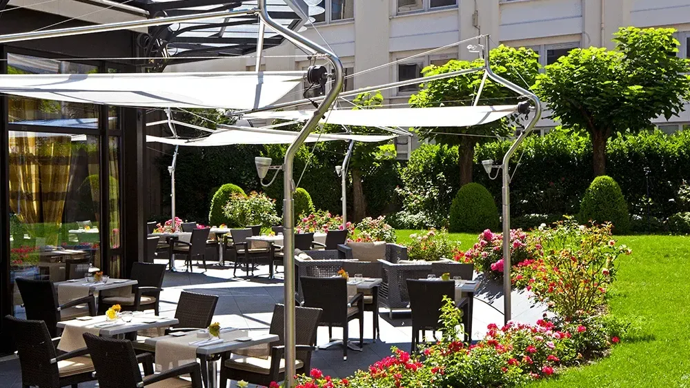 Outdoor hotel patio with white umbrellas & dining tables, and lush rose gardens at Warwick New York