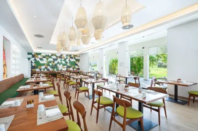 Intérieur lumineux et moderne du Market Café avec des chaises vertes et des tables en bois au Saint Martin Beach Resort & Spa
