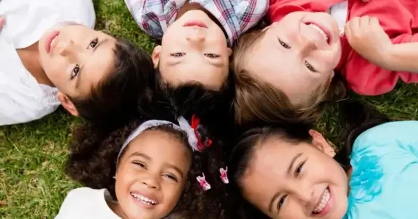 five young children smiling whilst lying down on grass