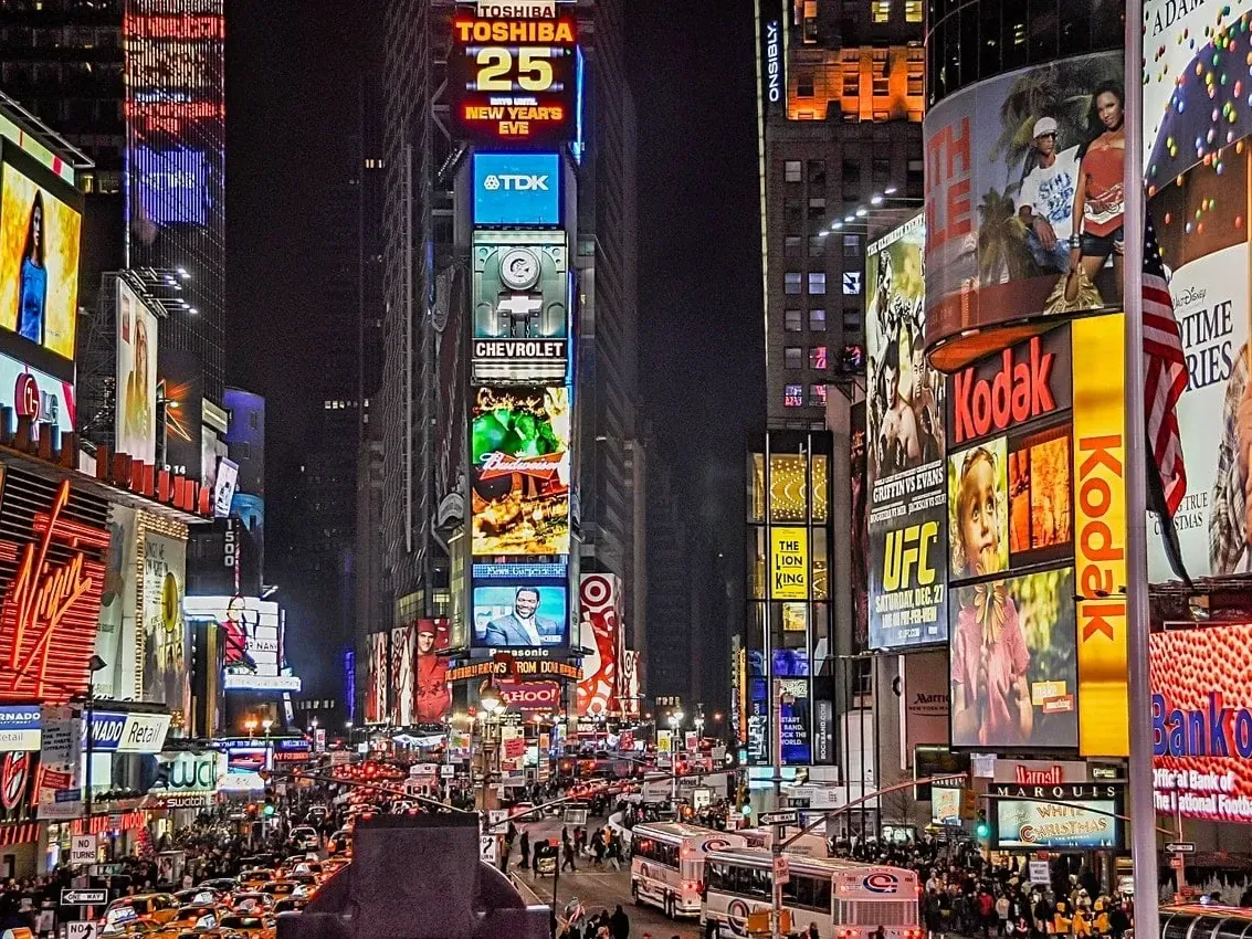 Bustling Times Square at night, filled with bright billboards, busy streets, and numerous taxis near Kixby Hotel