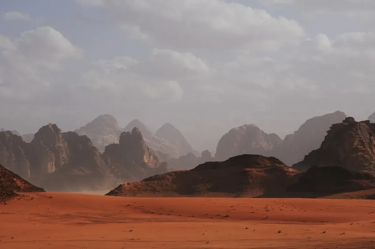 Red desert sands with rugged mountains rising in the haze