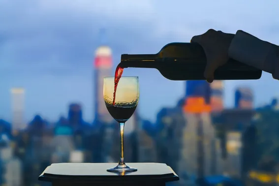 photo of glass of wine being poured with NYC view in the background
