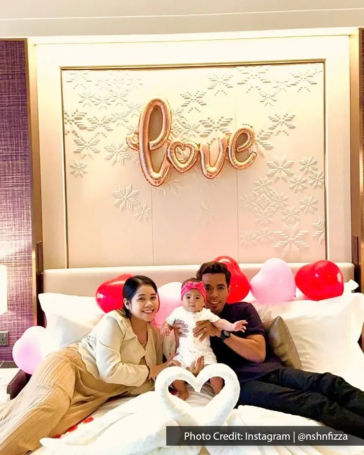 A couple sits on a bed, with a baby, sharing a joyful and intimate family moment together.