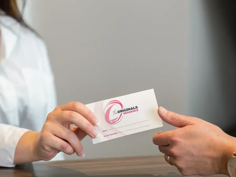 Two hands exchanging a card for The Originals Residence at Appart’Hôtel Hévéa.