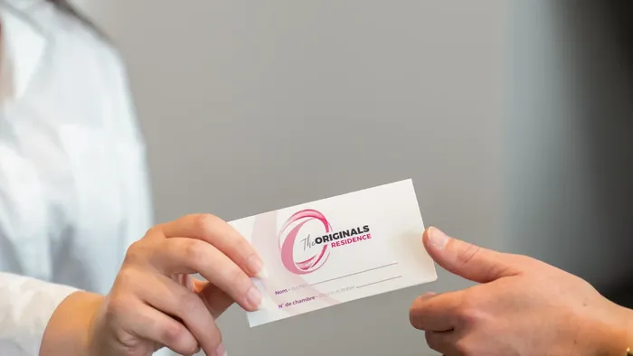Two hands exchanging a card for The Originals Residence at Appart’Hôtel Hévéa.