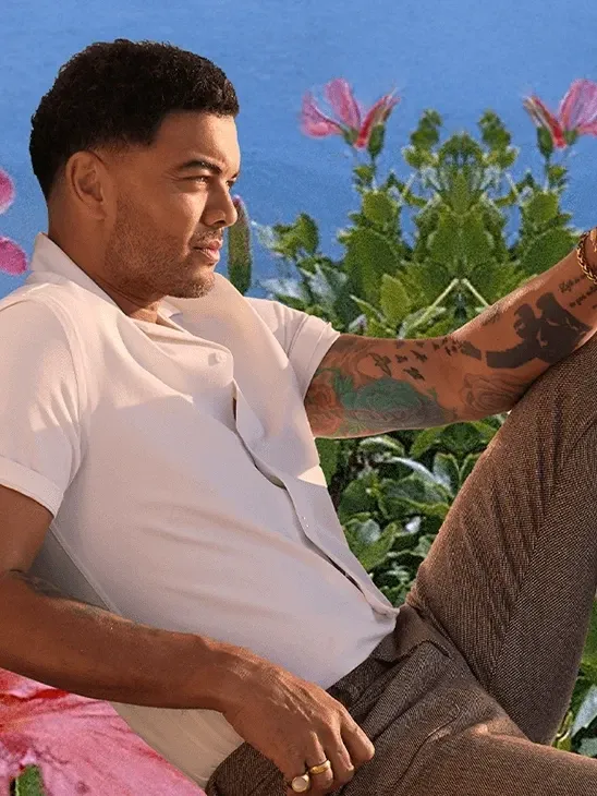 Guy Sebastian sitting on flowers with ocean in the background.