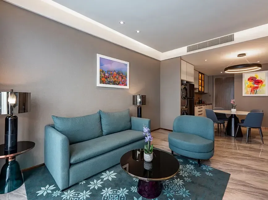 Modern living area with a blue sofa and dining table in the 2-Bedroom Suite at Imperial Lexis KL.