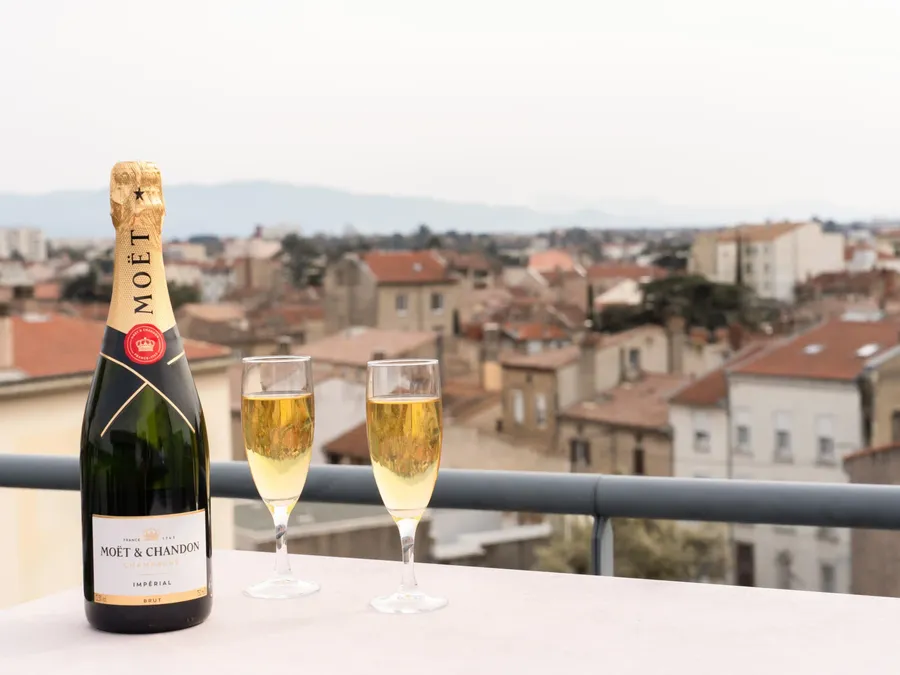 Bottle and two glasses of Moet & Chandon champagne on balcony overlooking cityscape.