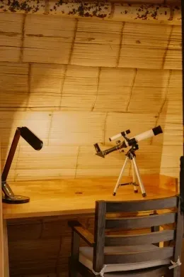 Telescope on a tripod by a wooden desk and chair beneath a bamboo ceiling at Unika Hotels, one of the best hotels in Bogota