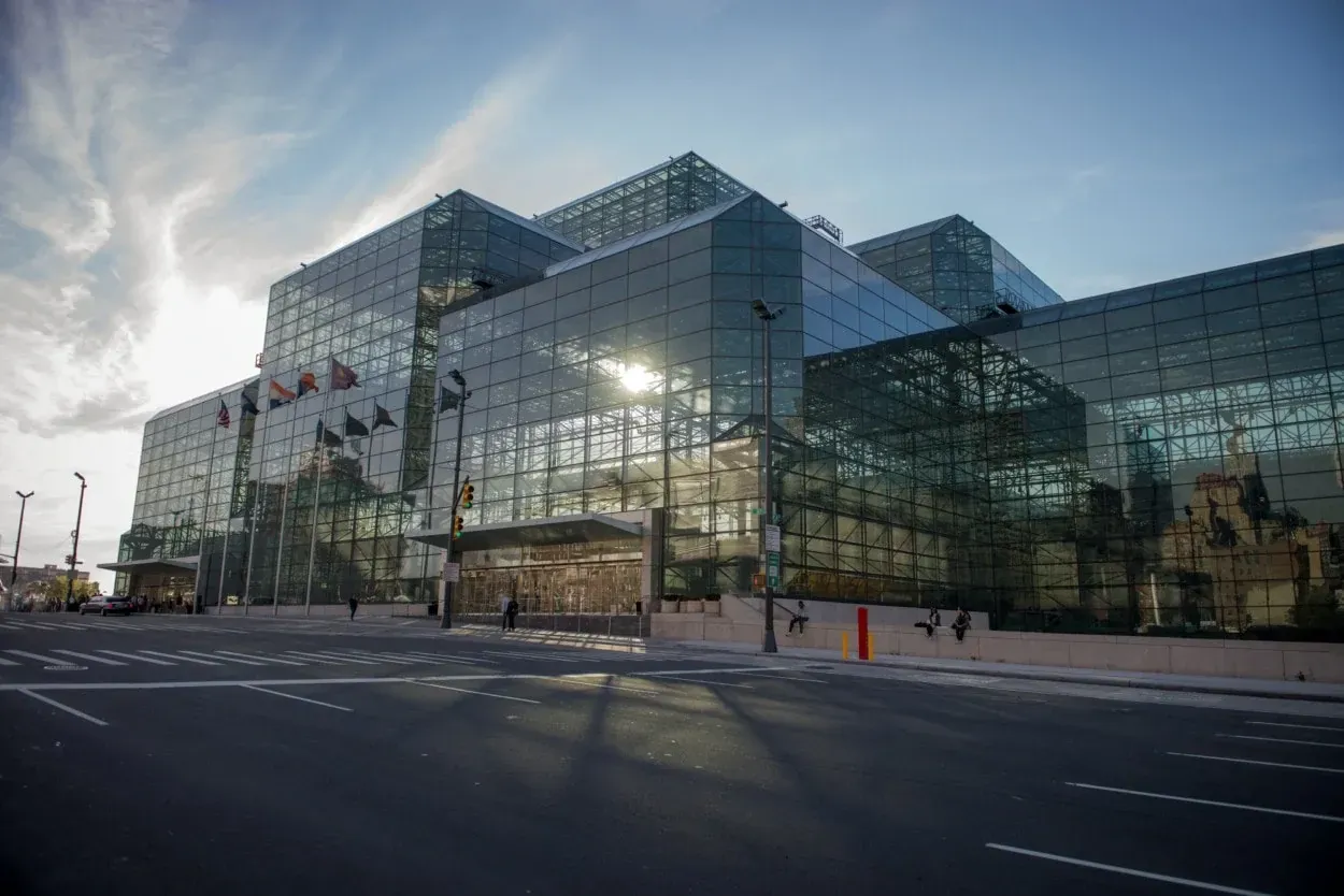 A large glass building with a modern design stands at a street corner with people walking by.