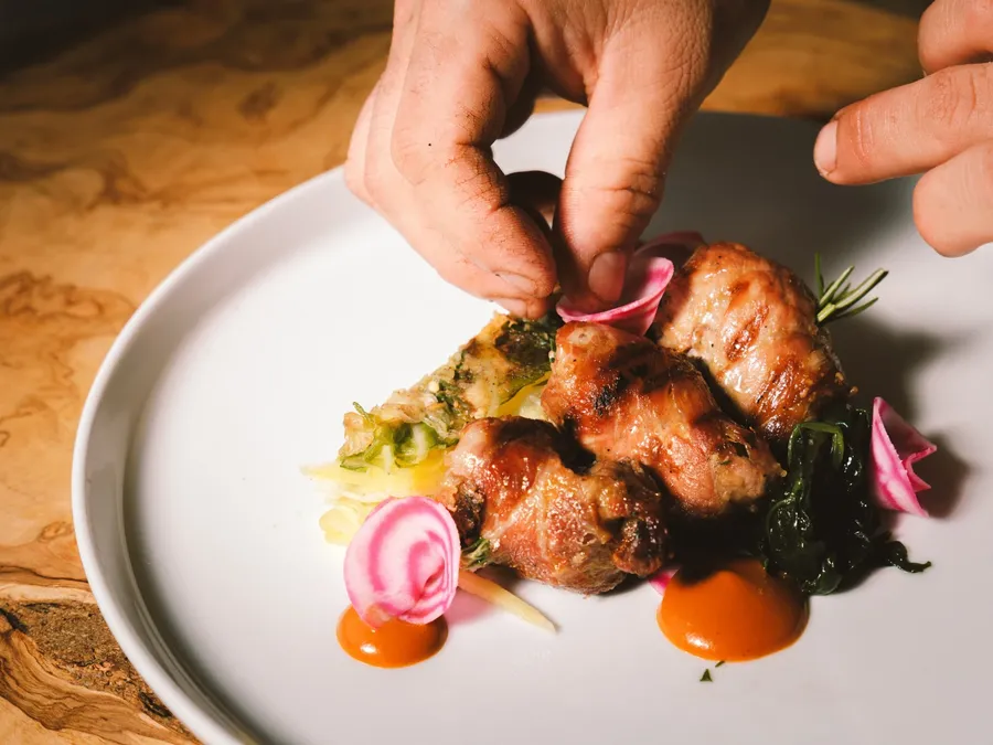 Mains préparant un plat de viande grillée sur une assiette blanche à Masseria Stali.
