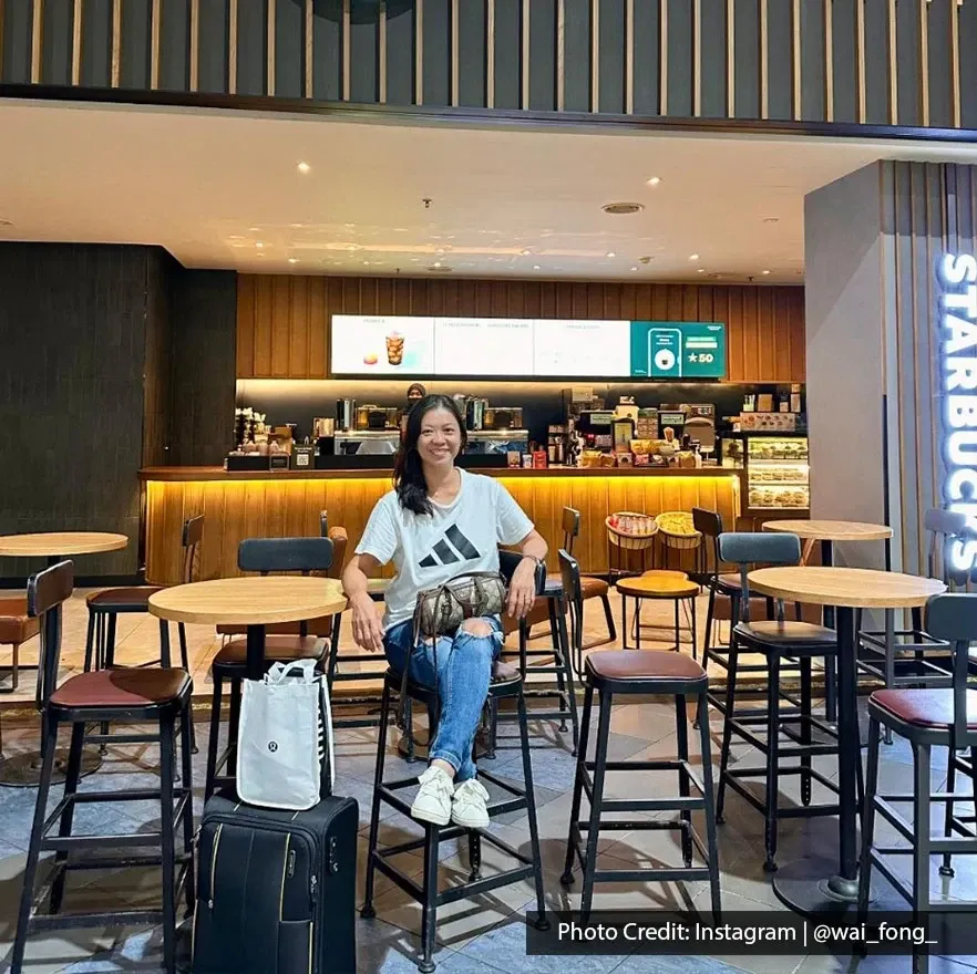 Woman sitting at Starbucks cafe inside Penang International Airport terminal with luggage beside her