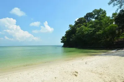 A sandy beach with lush trees lining the shore under a clear blue sky - Lexis Hibiscus Port Dickson