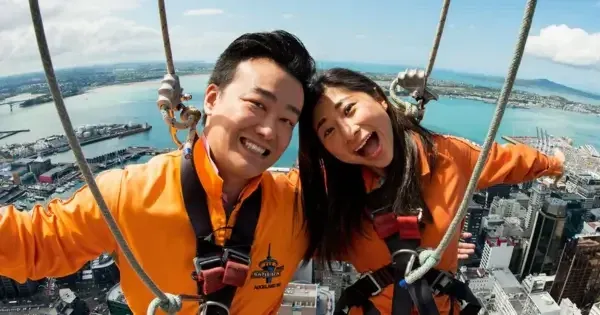 Two people in orange safety suits smiling during SkyWalk experience high above Auckland harbour