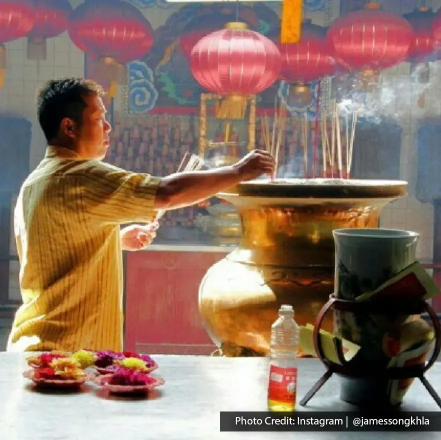Devotee offering prayers with incense burner inside Goddess of Mercy Temple in Penang.