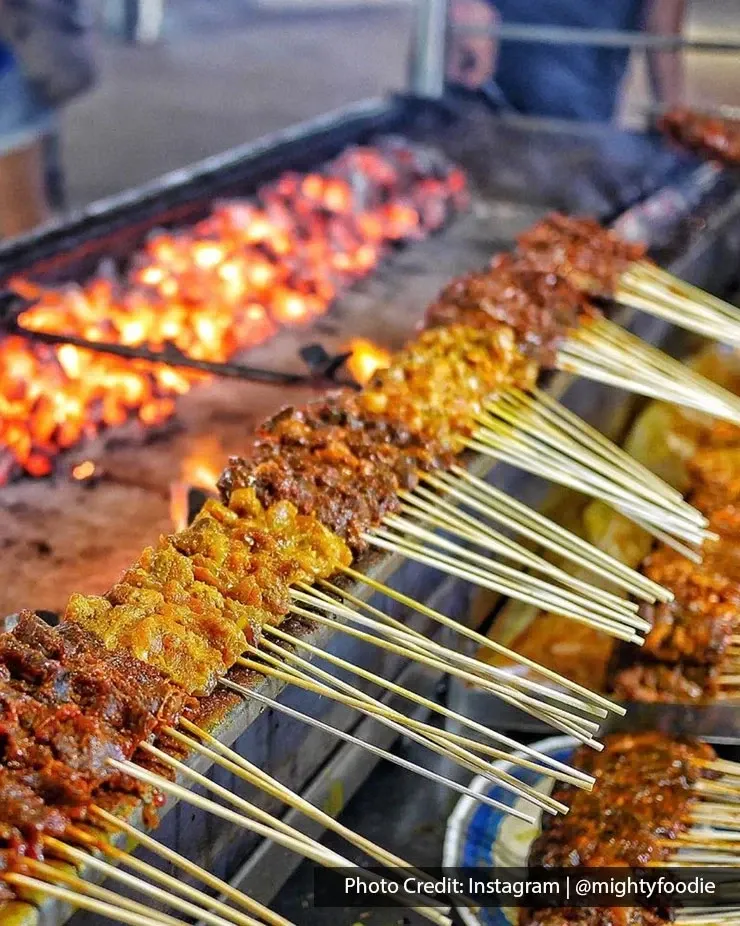 Satay skewers grilling over glowing charcoal.
