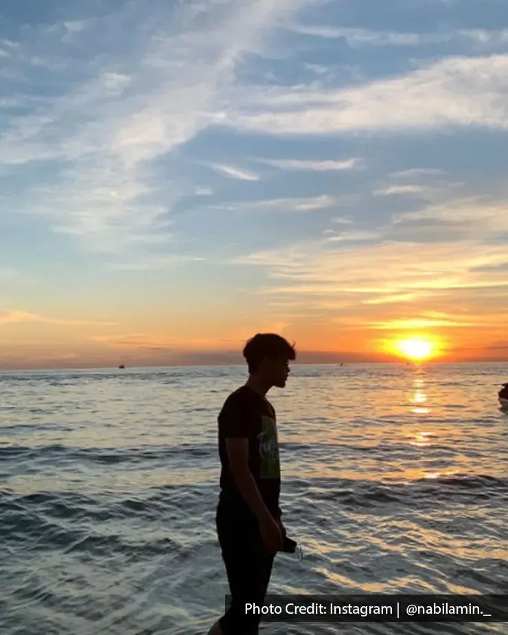 Seorang lelaki berjalan di tepi pantai menikmati pemandangan matahari terbenam indah di laut - Lexis Hibiscus Port Dickson