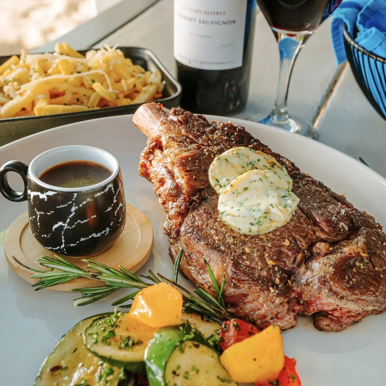 Omaha ribeye steak served with truffle parmesan French fries, grilled vegetables, rocket lettuce, red wine sauce, and herb compound butter.