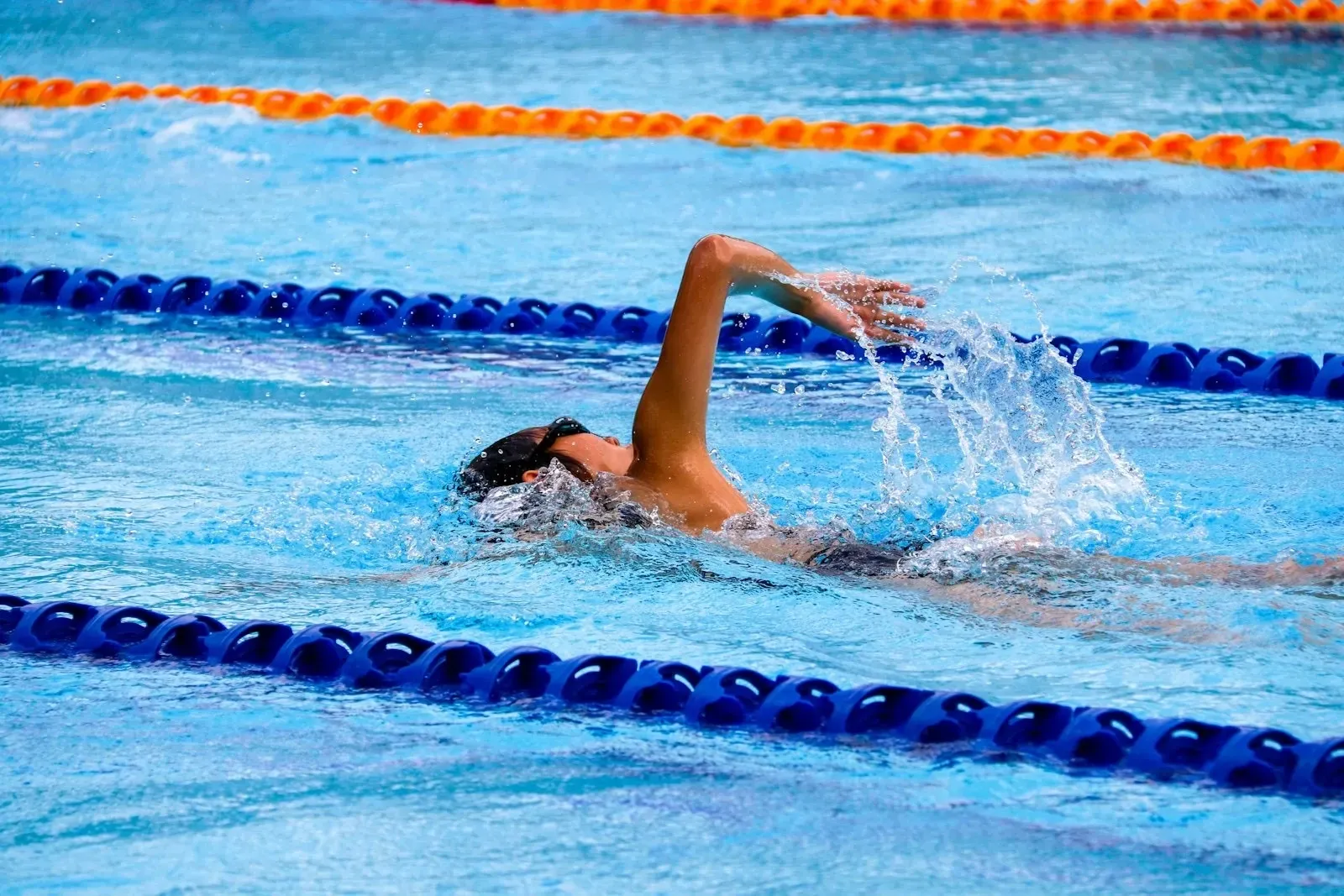 A swimmer mid-stroke between the lane ropes of a competition pool