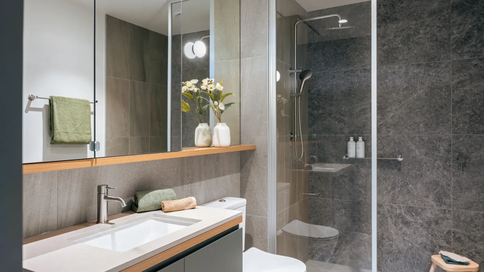 Modern bathroom with gray tiles, large mirror, sink, and shower.