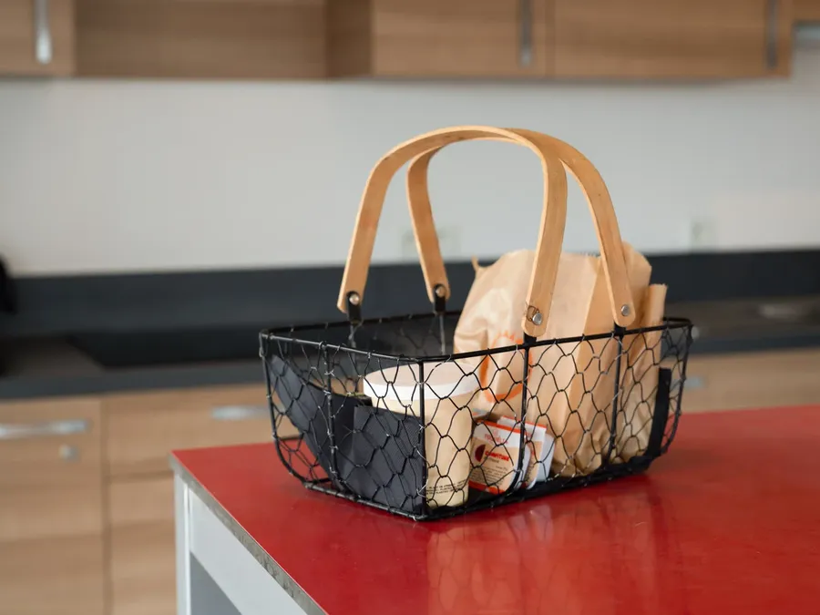 A basket with food on a red counter in a kitchen at Appart’Hôtel Hévéa.