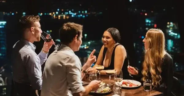 Four guests wine and dine at Orbit 360 Dining in the evening with city lights in background