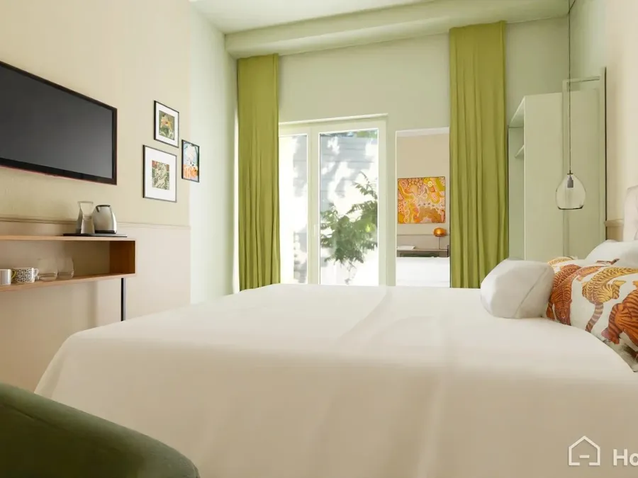 Chambre lumineuse avec lit double, rideaux verts et vue sur jardin au Flore Hôtel & Jardin