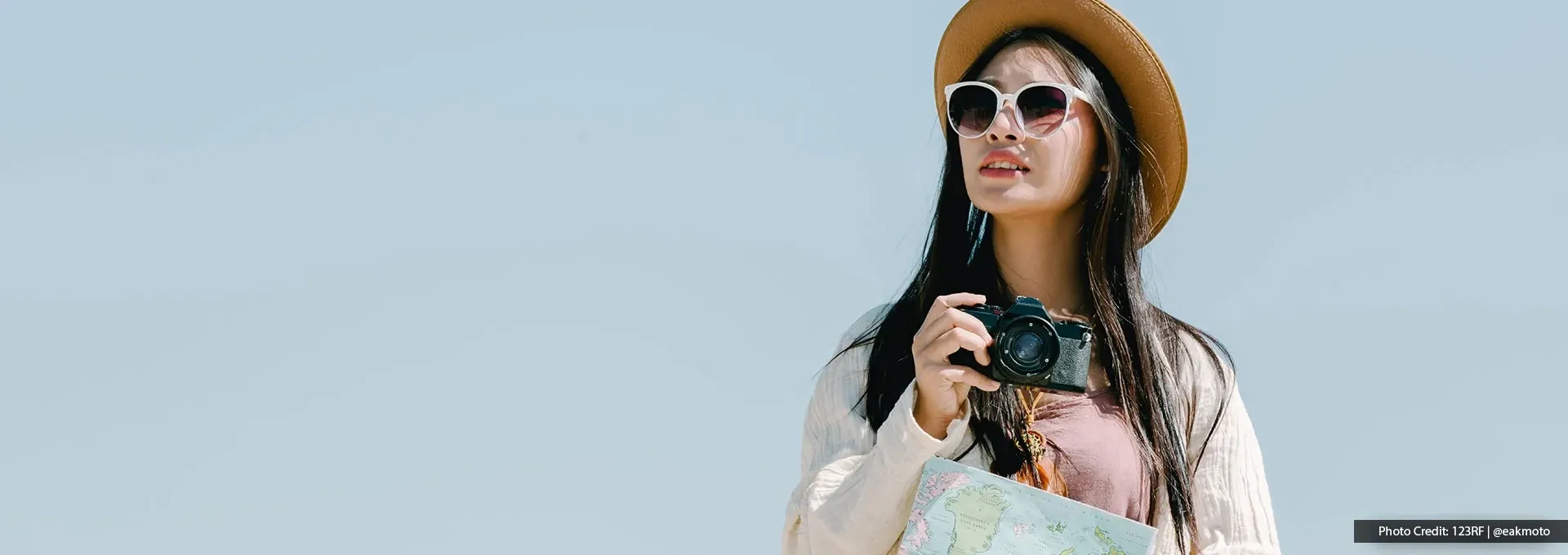 Person wearing sunhat holding camera and travel map.