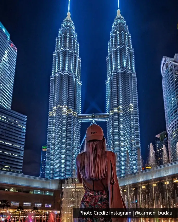 Person facing illuminated Petronas Twin Towers at night.