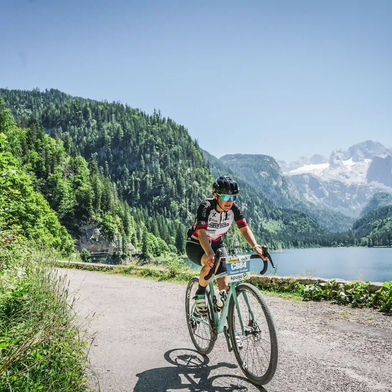 Radfahrer mit Nummerntafel C884 an einem See vorbei, Salzkammergut-Trophy 2026.