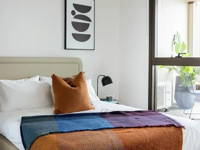 Modern hotel room with a cozy bed, colorful throws, and a balcony view at Caulfield Place.
