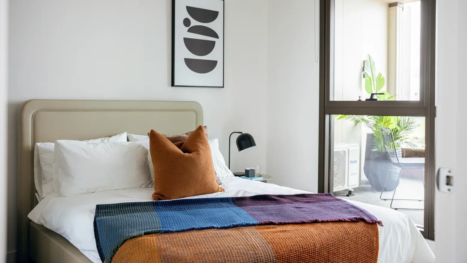 Modern hotel room with a cozy bed, colorful throws, and a balcony view at Caulfield Place.