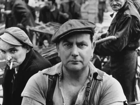 Black and white photograph showing workers in caps and overalls on a busy street at Caumont Centre d'Art