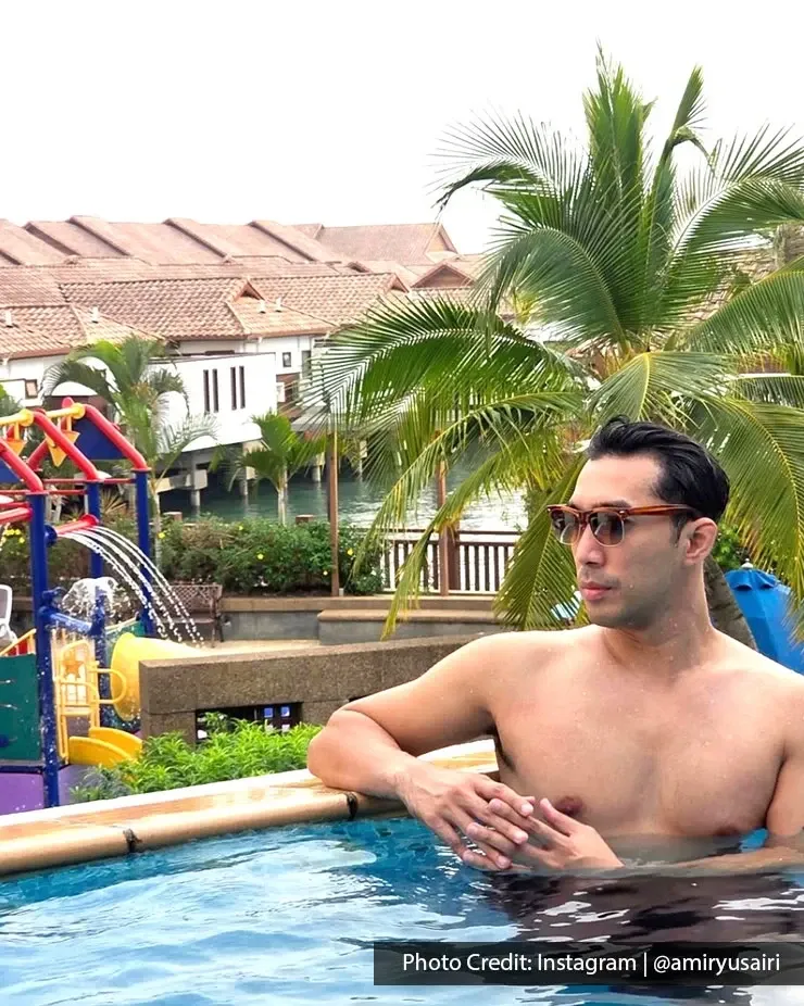 Man leaning beside outdoor pool with palm trees.