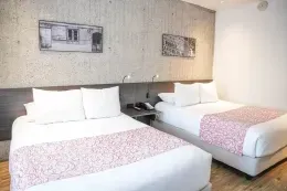 Two double beds with patterned runners against a textured grey accent wall under framed modern art inside Hotel B3 Virrey