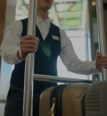 Bellhop in uniform pushing a luggage cart for a guest upon arrival or departure at The Whitehall Houston