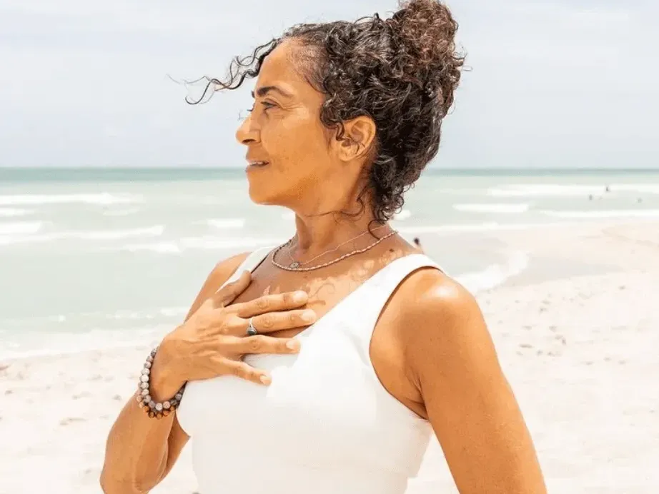 Woman facing the ocean with a hand over her chest near The Savoy Hotel & Beach Club