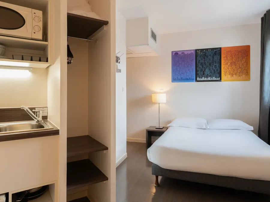 Standard Studio at Appart’Hôtel Hévéa in Valence with bed, lamp, sink, and microwave.