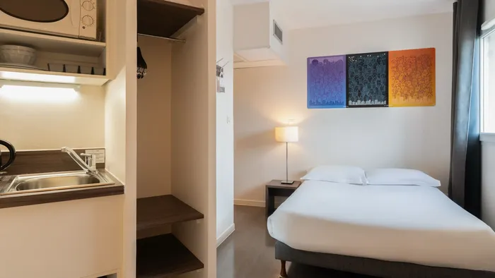 Modern bedroom with bed, lamp, sink, and microwave at Appart’Hôtel Hévéa.