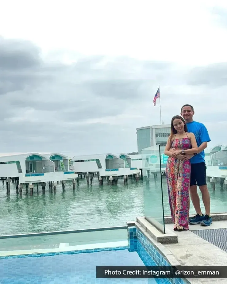 Smiling couple posing near an infinity pool overlooking luxury water villas.