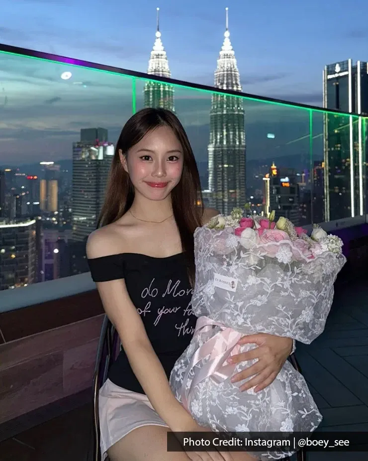 Chinese woman posing with a rose bouquet with Petronas Twin Towers lit up at night in the background.