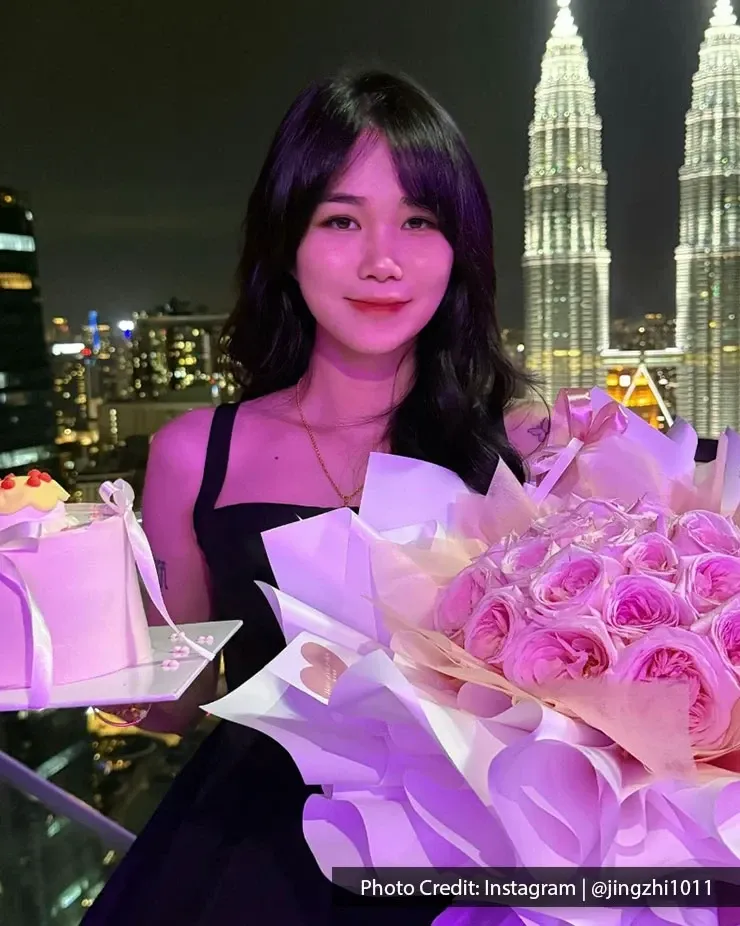 A woman holds a bouquet of flowers, with the Kuala Lumpur skyline visible in the background.