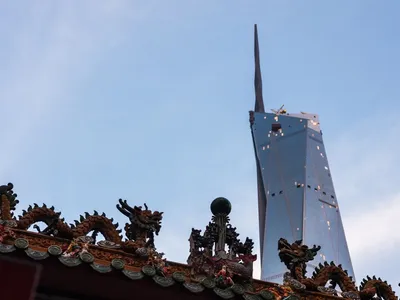 Dragon sculptures on a traditional roof against a blue sky with a modern skyscraper.